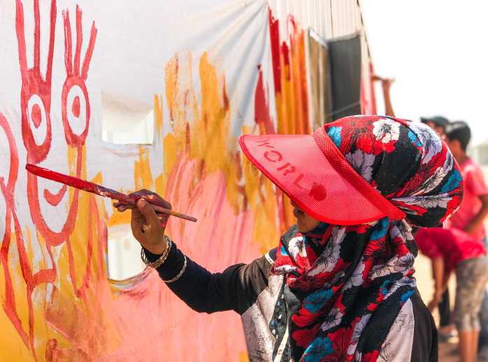 Noor works on a mural in her community in Azraq Camp